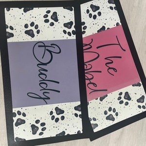 May include: Two black and white doormats with paw prints. The top mat has the text "The Rebel" in pink and the bottom mat has the text "Buddy" in purple.