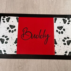 May include: Black and white paw print design doormat with a red centre panel that says "Buddy" in black cursive.