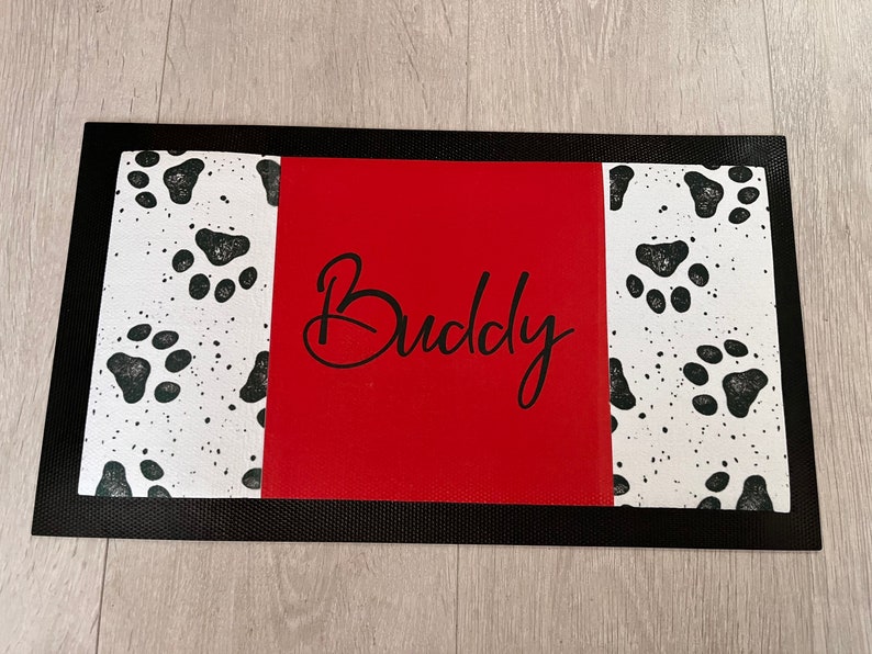 May include: Black and white paw print design doormat with a red centre panel that says "Buddy" in black cursive.