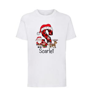 May include: White t-shirt featuring a festive Christmas design. The design includes a red and black plaid letter "S" with a Santa hat, along with Santa Claus, a snowman, a reindeer, and the name "Scarlet" in black.