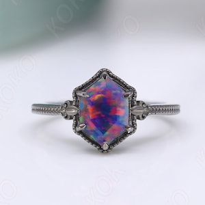 May include: A black ring with a hexagonal iridescent opal gemstone. The ring has a delicate design with small details.