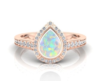May include: A pearlescent opal engagement ring set in rose gold with a pear-shaped stone surrounded by a halo of smaller diamonds. The band is also set with diamonds.