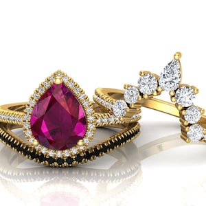 Op de afbeelding: Een verlovingsring met een peervormige robijn met een halo van diamanten, gezet in geel goud. De ring wordt geleverd met een bijpassende trouwring met zwarte diamanten.