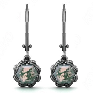 May include: A pair of silver-toned drop earrings. Each earring features a hexagonal, moss agate stone surrounded by a leaf-like design. The earrings have a lever-back closure.