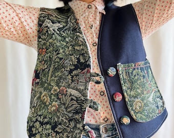 May include: A two-toned vest with a tapestry-like design on one side and a solid navy blue on the other. The tapestry side features a green and brown floral pattern. The vest has decorative buttons and a pocket.