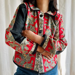 May include: A red, black and green patterned button-up shirt with a collar. The shirt has a floral design and is made of a lightweight fabric.