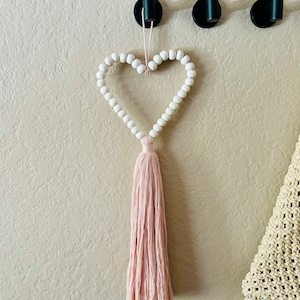 May include: A white beaded heart with a pink tassel hanging from a hook on a wall.