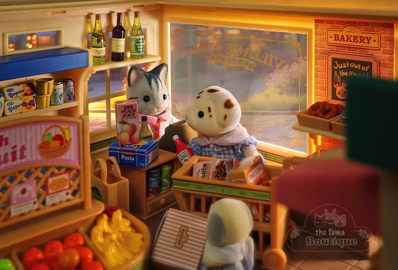 May include: A miniature toy grocery store and bakery scene. The store features shelves stocked with food items, a fruit stand, and a bakery with pretzels. Two animal figurines are present, one a cat and the other a dog, shopping in the store.