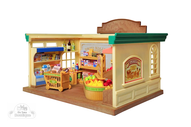 May include: A miniature toy grocery store with shelves stocked with food items, a shopping cart, and a bakery section. The store has a tan exterior with green trim and a brown roof. The bakery sign features illustrations of bread and pastries.