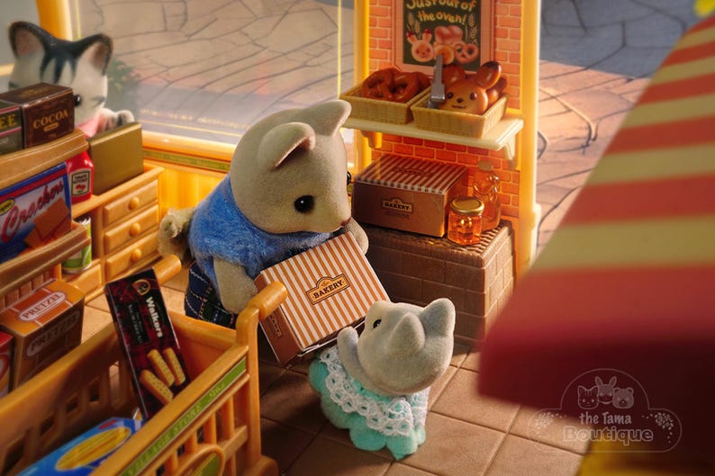 May include: A miniature bakery scene with animal figurines. A gray cat figurine looks over a shelf of snacks. Two bear figurines hold a bakery box. The bakery shelf displays baked goods and a sign that reads "Just out of the oven!"