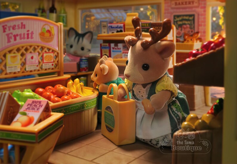 May include: A miniature grocery store scene with animal figurines. A deer figure holds a shopping bag. Baskets display fresh fruit, including tomatoes and bananas. A sign reads "Fresh Fruit". Other figures and shelves with products are visible.