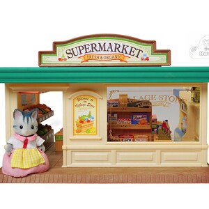 May include: A miniature toy supermarket with a green roof and a sign that reads "SUPERMARKET FRESH & ORGANIC". A gray cat figure in a pink dress and yellow apron stands in front of the store. The store has shelves with miniature food items.
