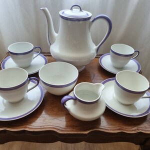 May include: A white tea set with purple trim. The set includes a teapot, creamer, sugar bowl, and four cups and saucers.