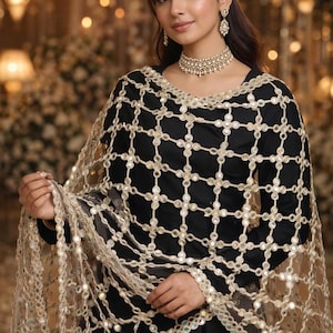 May include: A woman wearing a black dress and a sheer, gold-colored shawl with a grid pattern of small, reflective embellishments. The shawl is draped over the shoulders and arms. The woman is also wearing gold-colored jewelry.