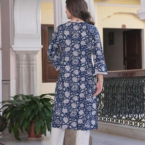 May include: A navy blue floral print tunic with three-quarter sleeves and white pants. The tunic features a white floral pattern and white lace trim on the sleeves. The outfit is completed with white heels.