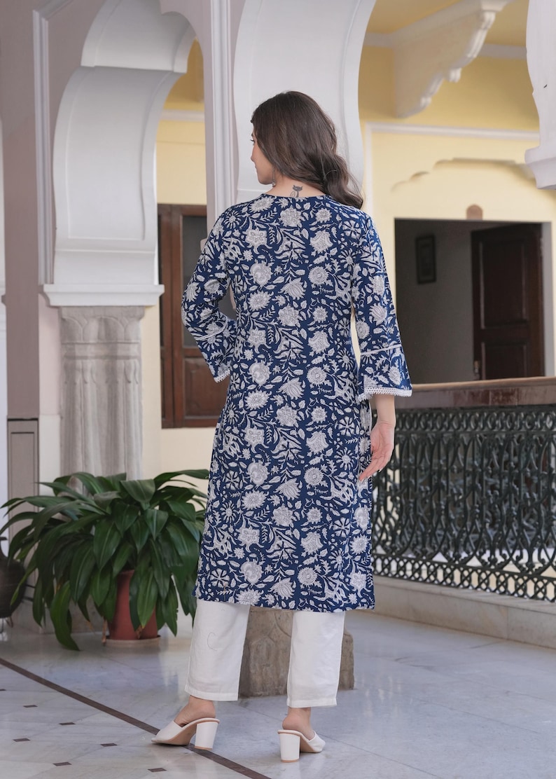 May include: A navy blue floral print tunic with three-quarter sleeves and white pants. The tunic features a white floral pattern and white lace trim on the sleeves. The outfit is completed with white heels.
