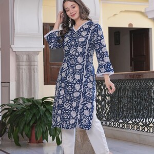 May include: A long-sleeved, navy blue tunic with a white floral pattern and white lace trim. The tunic is paired with white pants and white heeled sandals. The outfit is suitable for casual or semi-formal wear.
