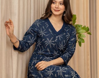 May include: A navy blue two-piece outfit with a white floral pattern. The top has a V-neck and three-quarter sleeves. The matching pants are visible. The outfit is worn by a person sitting on a wooden bench.