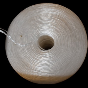 May include: A spool of white twine, tightly wound in concentric circles, against a black background. The twine has a slightly textured appearance, with a loose end extending from the side. Ideal for crafting and packaging.
