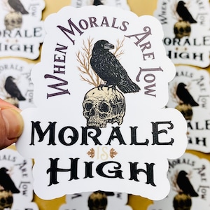 May include: A white sticker with a black crow perched on a skull. The sticker reads "When morals are low, morale is high".
