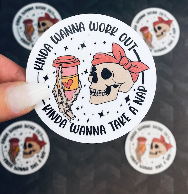 May include: A white round sticker with black text that reads "Kinda wanna work out - Kinda wanna take a nap". A cartoon skull with a pink bandana is holding a pink and white coffee cup. The sticker has a white background with black stars.