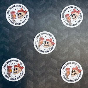 May include: Four white round stickers with a black skull holding a coffee cup with a pink heart on it. The text on the sticker reads "Kinda wanna work out - Kinda wanna take a nap".
