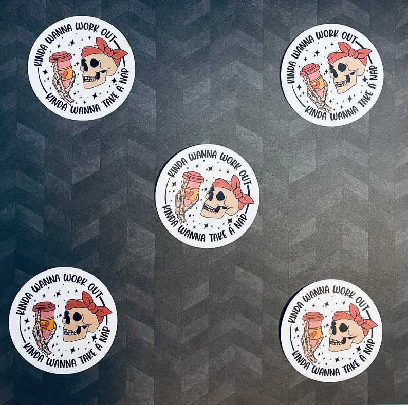 May include: Four white round stickers with a black skull holding a coffee cup with a pink heart on it. The text on the sticker reads "Kinda wanna work out - Kinda wanna take a nap".