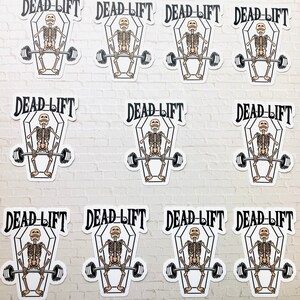 May include: Ten white stickers with a black and white illustration of a skeleton lifting a barbell inside a coffin. The text "DEAD-LIFT" is written above the coffin.
