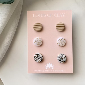 Op de afbeelding: Een set van zes kleioorbellen in verschillende patronen en kleuren. De oorbellen worden getoond op een roze kaart met de tekst "LOTUS OF CLAY HANDMADE JEWELRY & ACCESSORIES".