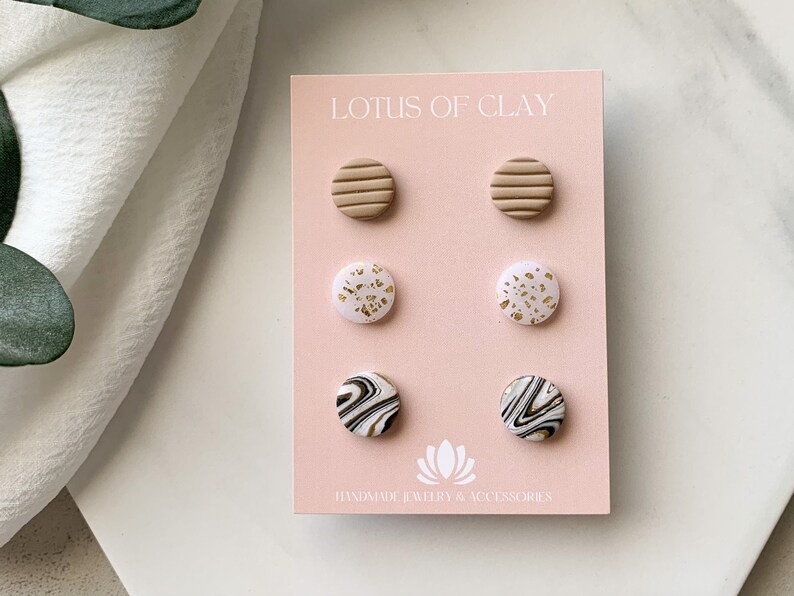 May include: A set of six clay earrings in a variety of patterns and colors. The earrings are displayed on a pink card with the text "LOTUS OF CLAY HANDMADE JEWELRY & ACCESSORIES".