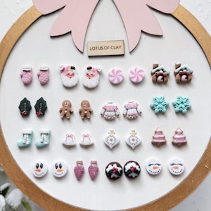 Könnte beinhalten: Eine Sammlung von Miniatur-Weihnachtsschmuck aus Ton, darunter Fäustlinge, Weihnachtsmann-Gesichter, Lebkuchenmänner, Pullover, Schneeflocken und Schneemänner. Die Ornamente sind auf einer weißen Oberfläche in einem Holzreifen angeordnet.