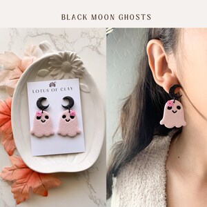 May include: Pink ghost earrings with black crescent moons and pink flowers. The earrings are on a white card with the text "LOTUS OF CLAY".