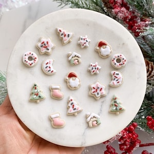 May include: A collection of 15 miniature Christmas-themed cookies, including a gingerbread house, a Santa Claus, a stocking, a donut, a star, a crescent moon, and Christmas trees. The cookies are decorated with white icing and red and green sprinkles.