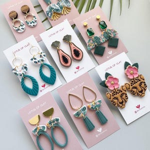 Op de afbeelding: Een verzameling handgemaakte oorbellen, gepresenteerd op roze kaarten. De oorbellen hebben verschillende ontwerpen, waaronder hout, bloempatronen, geometrische vormen en dierenprints. Het kleurenpalet omvat teal, goud, roze en bruin.