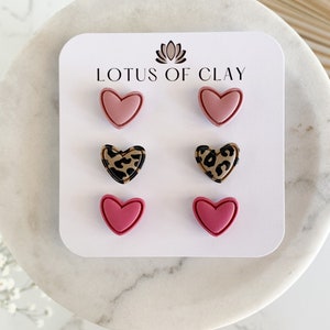 May include: Set of six heart-shaped earrings in pink and leopard print. The earrings are displayed on a white card with the text "LOTUS OF CLAY".