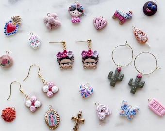 May include: A collection of miniature charms and earrings featuring various designs including a heart, a skull, a cross, a butterfly, cacti, flowers, and figures with floral headpieces. The items are crafted in colorful polymer clay and metal.