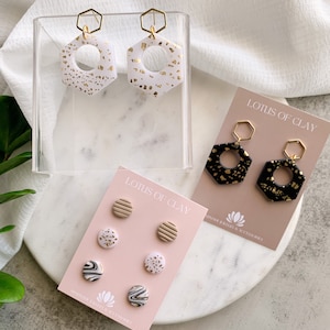 May include: A set of three pairs of handmade polymer clay earrings. The first pair is white with gold flecks, the second pair is black with gold flecks, and the third pair is a set of four small stud earrings with various patterns in white, black, and gold.