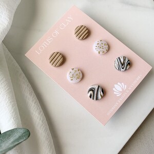 May include: A set of six clay earrings in a variety of patterns. The earrings are displayed on a pink card with the text "Lotus of Clay" and "Handmade Jewelry & Accessories".