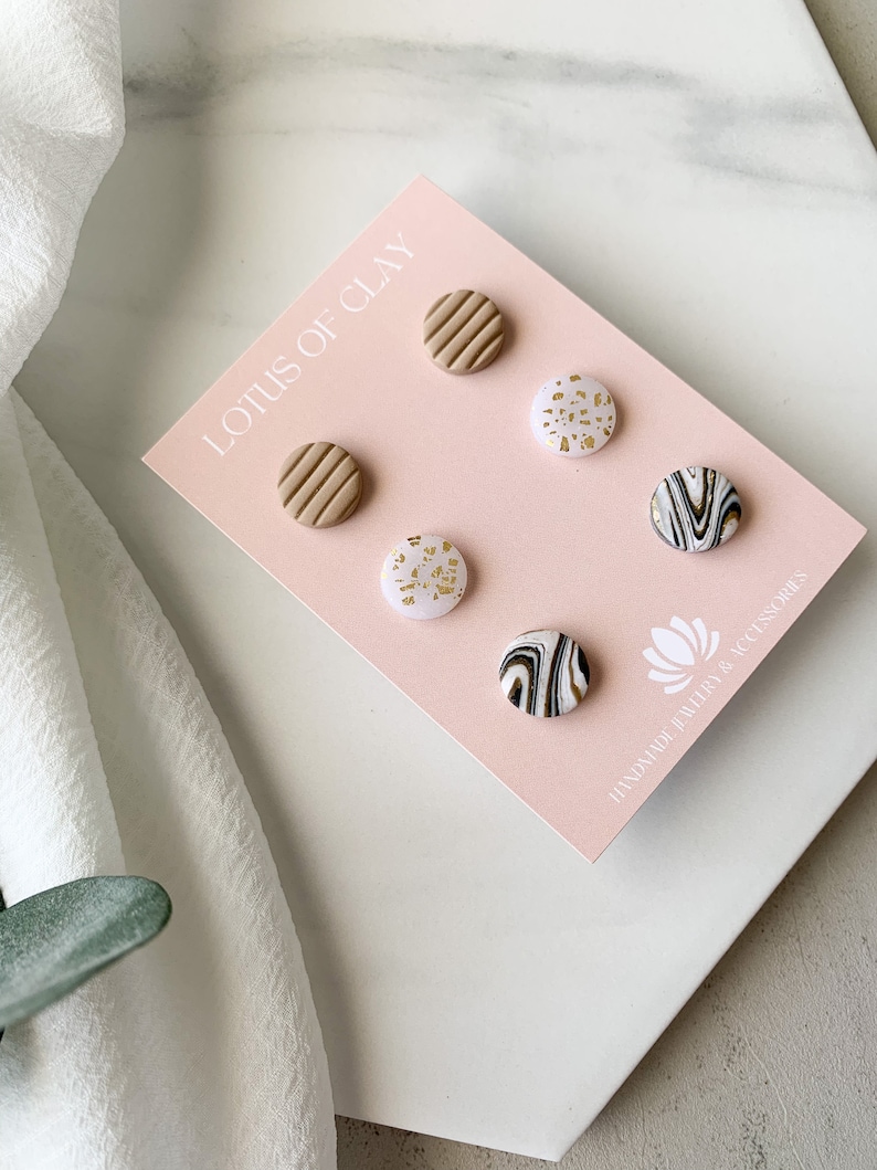 May include: A set of six clay earrings in a variety of patterns. The earrings are displayed on a pink card with the text "Lotus of Clay" and "Handmade Jewelry & Accessories".