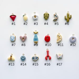 May include: A collection of seventeen colorful charms with gold-tone loops. The charms include a watermelon, lemon, flower, leaf, crescent moon, cactus, heart, fish, tomato, lemon slice, and more. Each charm is numbered.