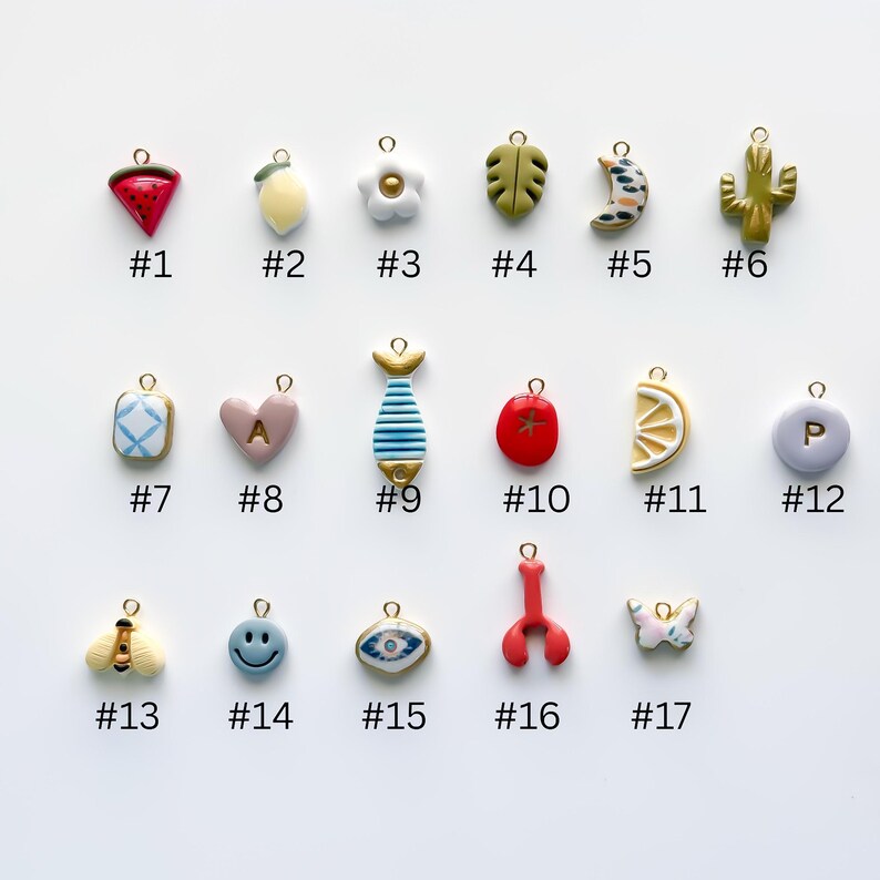 May include: A collection of seventeen colorful charms with gold-tone loops. The charms include a watermelon, lemon, flower, leaf, crescent moon, cactus, heart, fish, tomato, lemon slice, and more. Each charm is numbered.