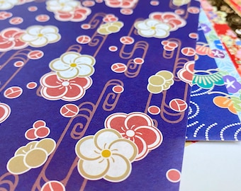 May include: A stack of colourful patterned origami paper with a blue floral design on top. The paper has a repeating pattern of white and red flowers with gold accents.