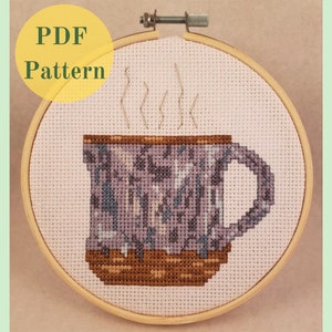Può includere: Uno schema a punto croce di una tazza viola e marrone con vapore che esce dalla parte superiore. La tazza è su uno sfondo bianco.