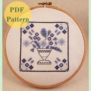 May include: A blue and white cross stitch pattern of a vase with flowers, framed in a wooden embroidery hoop. The pattern is titled "PDF Pattern".