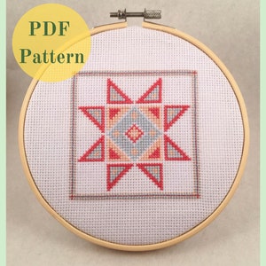 May include: A cross-stitch pattern in a wooden embroidery hoop. The design features a geometric star pattern in red, peach, and blue on a white background. The text "PDF Pattern" is in a yellow circle.