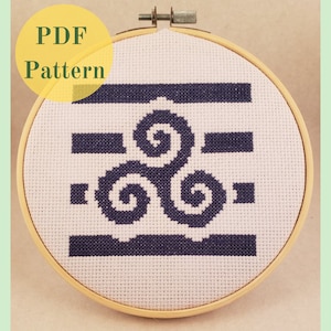 Peut inclure: Un cerceau de broderie blanc avec un motif de point de croix bleu et blanc représentant un motif de triple spirale stylisé. Le motif est entouré d'une bordure noire. Le cerceau est étiqueté "PDF Pattern".