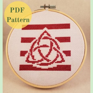 May include: A white embroidery hoop with a red and white cross stitch pattern. The pattern features a red Celtic knot design with three interlocking circles.