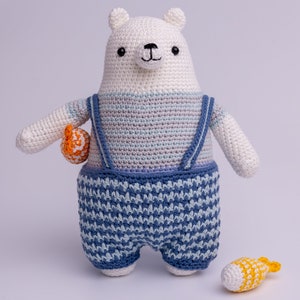 May include: A white crocheted polar bear wearing blue and white striped overalls and holding an orange crocheted fish. A yellow crocheted fish is on the floor.