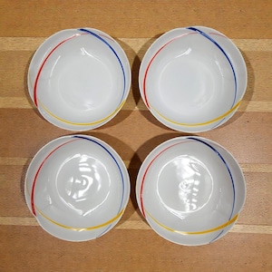 May include: Four white ceramic bowls with a colorful design. Each bowl has a red, blue, and yellow stripe pattern. The bowls are arranged on a light brown wooden surface.