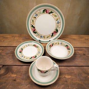 May include: A vintage white ceramic dish set with a green and gold border. The set includes a large plate, two smaller plates, a bowl, and a teacup with saucer. The plates and cup feature a floral and fruit design.